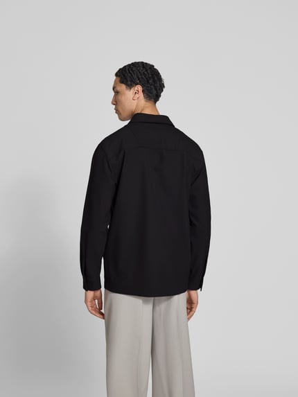 Männermodel trägt Freizeithemd mit Brusttasche von Closed in Schwarz, lockerer Schnitt, glatter Stoff, Rückenansicht, Ganzkörperansicht Rückansicht.