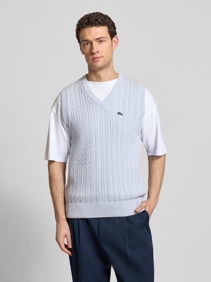 Männermodel trägt Regular Fit Pullunder aus Baumwoll-Mix von Lacoste in Hellblau, Zopfmuster, Strickoptik, Logo-Detail, Ganzkörperansicht von vorne.