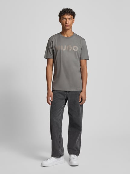 Męski model trägt Relaxed Fit T-Shirt aus reiner Baumwolle Modell 'DULIVIO' von HUGO, efekt: jednolity kolor, z napisem z logo, okrągły dekolt, rękaw: krótki rękaw, wykończenie materiału: dżersej, materiał: bawełna, Ganzkörperansicht von vorne