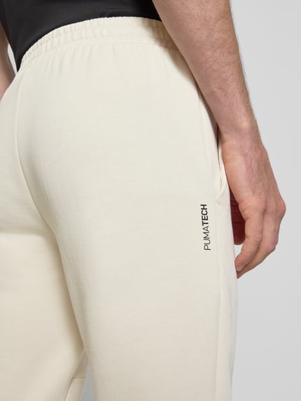Männermodel trägt Regular Fit Sweathose mit Logo-Print Modell 'Pumatech' von PUMA PERFORMANCE, cremefarben, Baumwoll-Mix, Detailaufnahme Oberschenkel.