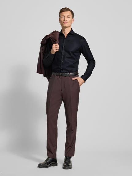 Männermodel trägt Slim Fit Businesshemd mit extra langem Arm Modell 'HANK' von BOSS in Unifarben, feines Strukturmuster, Ganzkörperansicht von vorne.