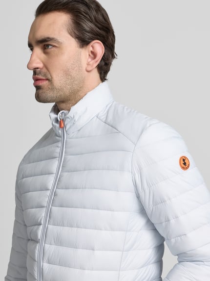 Männermodel trägt Steppjacke mit Zweiwegereißverschluss Modell 'Alexander' von SAVE THE DUCK in Stepp-Optik, Nahaufnahme Oberkörper, Regular Fit, hellgraue Farbe, glatte Textur, Sichtbarkeit des Markenlogos.