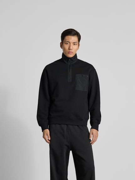 Mężczyznę model nosi Troyer aus reiner Baumwolle od MAISON KITSUNÉ, czarny, krój regular fit, kołnierz zapinany, detal z logo, brustasza, długość tyłu w rozmiarze M: 68 cm, pełen widok z przodu