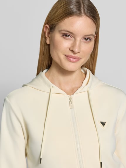 Frauenmodel trägt Sweatjacke mit Label-Applikation Modell 'OLYMPE' von Guess Activewear in Creme, glatte Textur, Nahaufnahme Oberkörper.