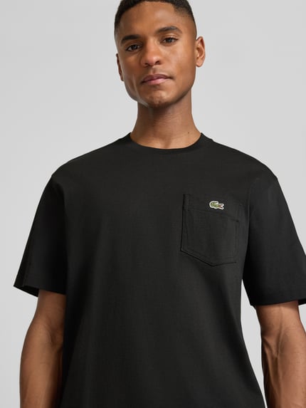 Männermodel trägt Regular Fit T-Shirt aus reiner Baumwolle von Lacoste, unifarben schwarz mit Logo-Stitching, Nahaufnahme Oberkörper.