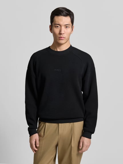 Męski model nosi Regular Fit Sweatshirt aus reiner Baumwolle Modell 'DAFFLYN' od HUGO, czarny, strukturalny wzór, label stitching, długi rękaw, dekolt okrągły, żakardowa bawełna, całkowity widok z przodu.