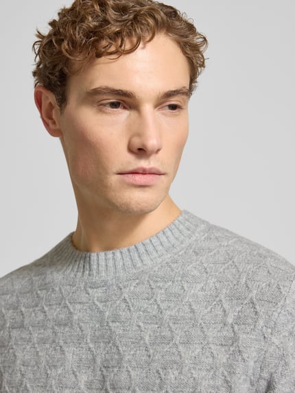 Męski model nosi szary Strickpullover mit gerippten Abschlüssen Modell 'BLASIMON' od Jack & Jones Premium, zbliżenie na górną część ciała.
