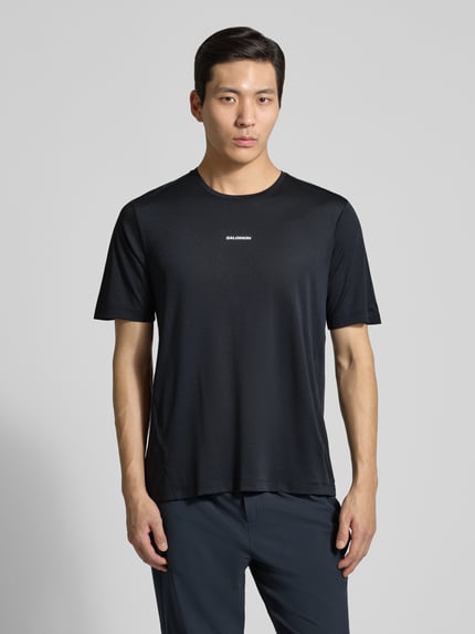 Männermodel trägt T-Shirt mit Rundhalsausschnitt und Logo von Salomon in Schwarz, Regular-Fit, Rückenlänge 69 cm bei Größe M, Ganzkörperansicht von vorne