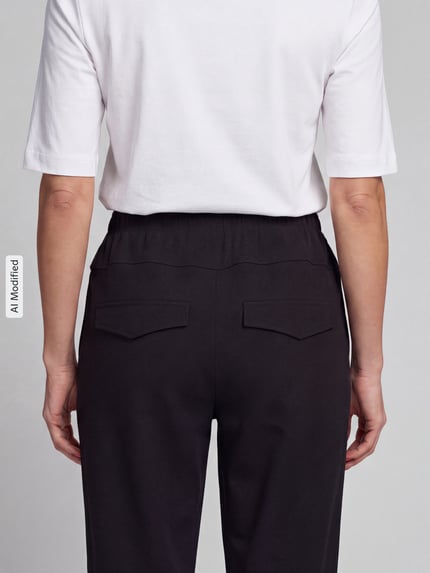 Frauenmodel trägt Barrel Leg Hose mit angedeuteten Taschen Modell 'Rachell' von Stehmann in unifarbenem Schwarz, elastischer Mid Waist Bund, Sweat-Material, Ganzkörperansicht Rückansicht, KI-modifiziertes Bild.