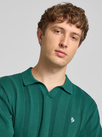 Mężczyznamodel nosi Regular Fit Poloshirt mit Logo-Stitching od REVIEW, z bawełny, wyhaftowane logo, ażurowy haft, krótki rękaw, długość tyłu 56 cm w rozmiarze M, zbliżenie na górną część ciała.