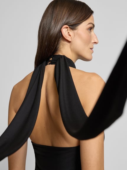 Frauenmodel trägt Jumpsuit mit Neckholder von Mango in Schwarz, Material-Mix mit Stretch, lockerer Schnitt, Detailaufnahme Rückenansicht.