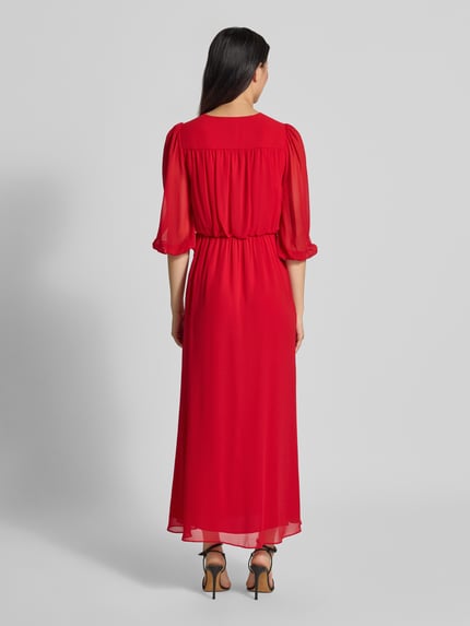 Vrouwenmodel draagt avondjurk van chiffon in rood, getailleerde pasvorm, tailleband, 3/4-mouw, Maxilengte, onderrok, Model 'Heather' van Forever New, geheellichaamsaufnahme achterkant.
