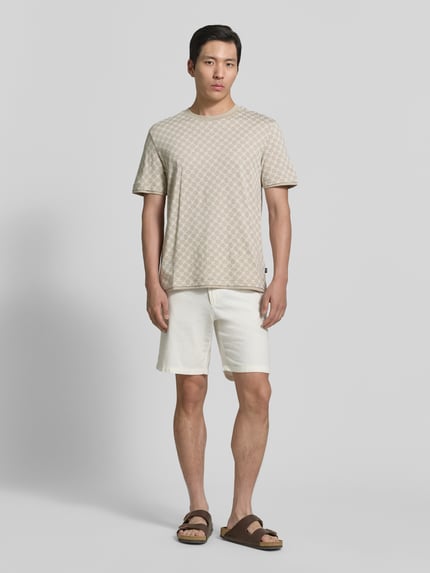 Männermodel trägt T-Shirt mit Logo-Muster und Rundhalsausschnitt von JOOP! Collection aus Baumwoll-Lyocell-Mix, Regular-Fit, Beige auf Weiß, glatte Textur, Rückenlänge bei Größe M: 69 cm, Ganzkörperansicht von vorne.