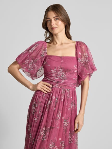 Frauenmodel trägt Abendkleid mit Karree-Ausschnitt von LACE & BEADS aus pinkem Chiffon mit floralem Muster, Ballonärmel, Nahaufnahme Oberkörper.