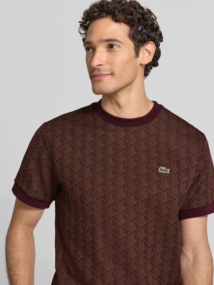 Männermodel trägt Regular Fit T-Shirt aus Baumwoll-Mix von Lacoste in Braun mit geometrischem Muster, Nahaufnahme Oberkörper. Herren T-Shirt von Lacoste.