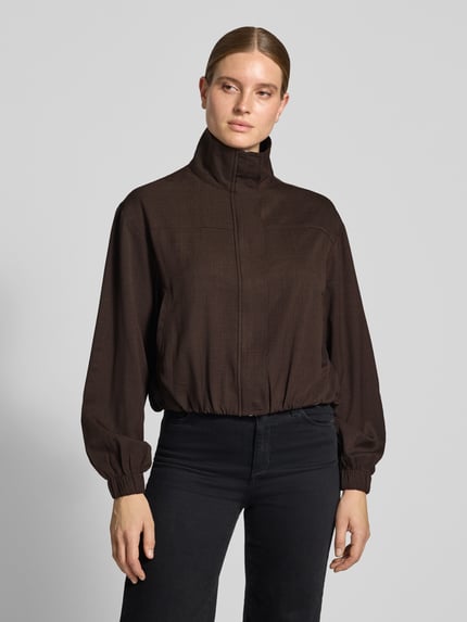 Frauenmodel trägt Regular Fit Jacke mit Stehkragen Modell 'Felicity' von Neo Noir in Dunkelbraun, leicht glänzende Struktur, Ganzkörperansicht von vorne. Rückenlänge 52 cm, Schulterbreite 54 cm, Brustweite 54 cm, Ärmellänge 60 cm.