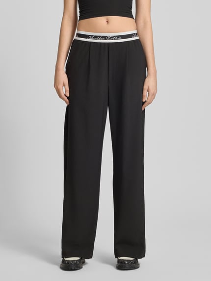 Frauenmodel trägt Wide Leg Hose mit elastischem Logo-Bund von ANOTHER COTTON LAB in Schwarz mit weißen Details, Material-Mix mit Stretch und Eingrifftaschen, Nahaufnahme Oberkörper.