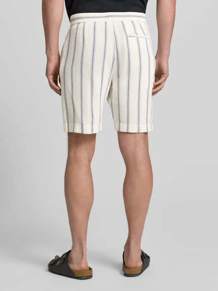 Männermodel trägt Regular Fit Shorts aus reiner Baumwolle Modell 'REGCAL' von SELECTED HOMME, cremefarben mit blauen Streifen, Strukturstoff, Ganzkörperansicht Rückansicht.
