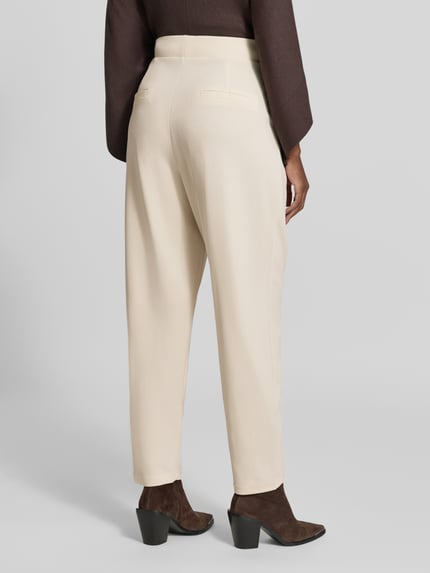 Frauenmodel trägt Relaxed Fit Anzughose mit Bundfalten Modell 'SC-SIHAM 103' von Soyaconcept in Beige, glatte Textur, Ganzkörperansicht Rückansicht. Damen Anzughose von Soyaconcept.