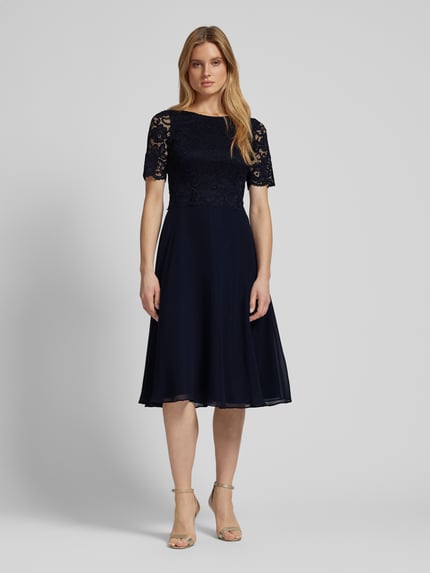 Frauenmodel trägt Cocktailkleid mit Spitzenbesatz von Vera Mont im unifarbenen Design, taillierter Schnitt, Material-Mix mit Stretch-Anteil, blickdichtes Unterkleid, Nahtreißverschluss, Rückenlänge 116 cm, Brustweite 45 cm, Ärmellänge 32 cm, Ganzkörperansicht von vorne.