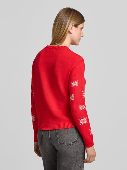 Frauenmodel trägt Pullover mit Pailletten-Schriftzug von VERO MODA in Rot mit weißem Sternenmuster, Strickoptik, Ganzkörperansicht Rückansicht.