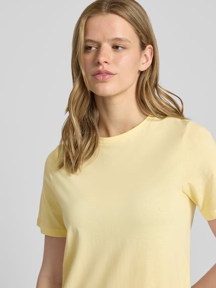 Frauenmodel trägt Regular Fit T-Shirt-Kleid aus reiner Baumwolle Modell 'DISSO' von Pieces in unifarbenem Hellgelb, Nahaufnahme Oberkörper.