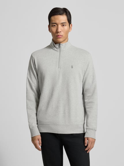 Männermodel trägt Sweatshirt mit Label-Stitching von Polo Ralph Lauren aus Baumwoll-Viskose-Mix, lockerer Schnitt, Stehkragen, kurzer Reißverschluss, gerippte Abschlüsse, Rückenlänge 69 cm, Ärmellänge 64 cm, hellgrau-meliert, Ganzkörperansicht von vorne.