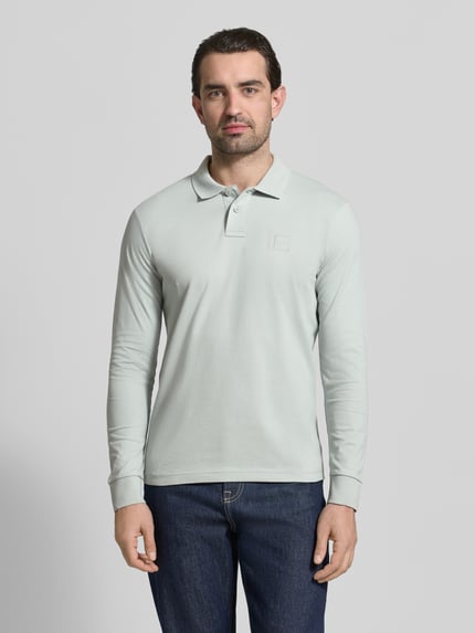 Männermodel trägt Slim Fit Poloshirt aus katoenmix Modell 'PASSERBY' van BOSS Orange, effen, lange mouw, label stitching, piqué textuur, voorkant volledige lichaamsweergave.