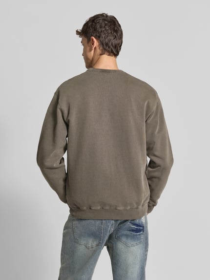 Męski model nosi Sweatshirt mit Label-Stitching von Forét z bawełny ekologicznej, prosty krój, okrągły dekolt, prążkowane wykończenia, długość tyłu w rozmiarze M: 68 cm, widok całej sylwetki z tyłu.