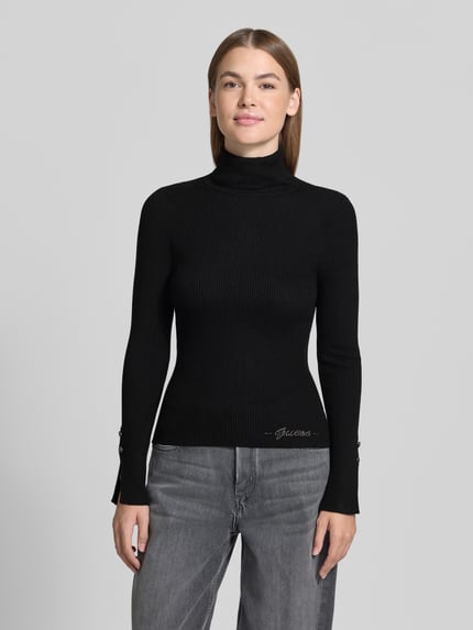 Vrouwenmodel draagt zwarte Strickpullover aus Viskose-Mix mit Rollkragen van GUESS, slim fit, ripp structuur, labeldetail, voorkant totaalbeeld.