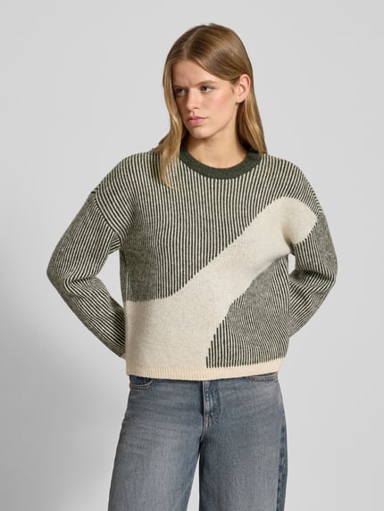 Frauenmodel trägt Loose Fit Strickpullover mit Allover-Muster Modell 'LINNA' von Pieces, gestreift, Rundhals, Stricktextur, Ganzkörperansicht von vorne.
