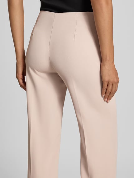 Vrouwenmodel draagt Flared Fit broek met bandplooien van Rinascimento, elastische materiaalmix, naadritssluiting, binnenbeenlengte maat S 85 cm, bandwijdte maat S 37 cm, kleur lichtbeige, gladde stof, Ganzkörperansicht Rückansicht.