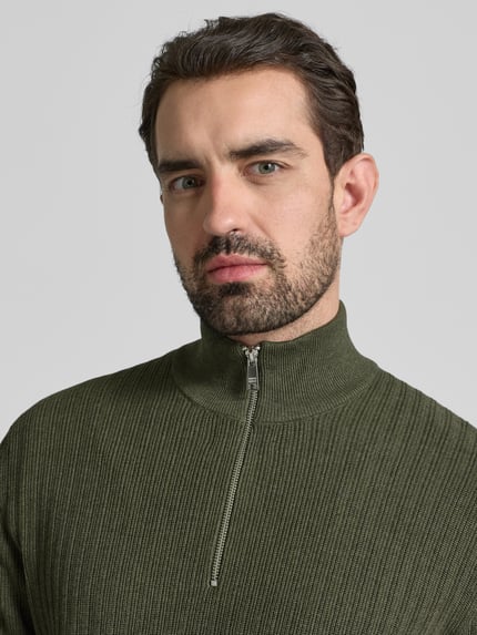 Männermodel trägt Strickpullover mit gerippten Abschlüssen von Christian Berg Men in olivgrün, katoen, korte rits, nahaufnahme oberkörper.