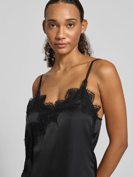 Modelka kobieca nosi czarne A-Linie Freizeitkleid mit Spitzenbesatz Modell 'ELVA' od PIECES, jednolity, z koronkowymi detalami, spaghettiträger, asymetryczne wykończenie dołu, tkanina o jedwabistym połysku, zbliżenie na górną część ciała.