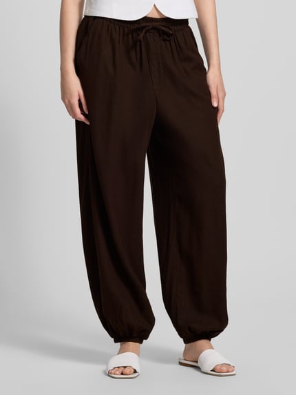 Frauenmodel trägt Regular Fit Weite Hose aus Viskose-Leinen-Mix Modell 'GOA' von Only, Optik: Unifarben, Materialverarbeitung: Flammgarn, Tunnelzug, Bundabschluss und Beinabschluss elastisch, seitliche Eingrifftaschen und Gesäßtasche, Farbe Braun, Nahaufnahme Unterkörper.