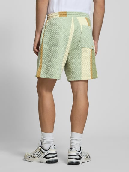 Männermodel trägt Straight Fit Shorts mit Strukturmuster von BLKVIS in Mint mit Creme und Ocker, Elastischer-Material-Mix, Gesäßtasche, Ganzkörperansicht Rückansicht.