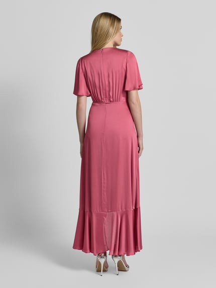 Modelka nosi Abendkleid in Wickel-Optik mit Bindegürtel od Christian Berg Cocktail, różowy satynowy materiał, talia podkreślona, długość maxi, dekolt V, pasek do wiązania, dół z falbaną, długość pleców w rozmiarze 36: 141 cm, szerokość w rozmiarze 36: 32 cm, długość rękawa w rozmiarze 36: 28 cm, widok całej sylwetki z tyłu.