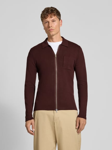 Männermodel trägt Regular Fit Strickjacke aus Viskose-Mix Modell 'GUNA' von Samsøe Samsøe in Dunkelrot, Zweiwege-Reißverschluss, Brusttasche, Umlegekragen, Ganzkörperansicht von vorne.