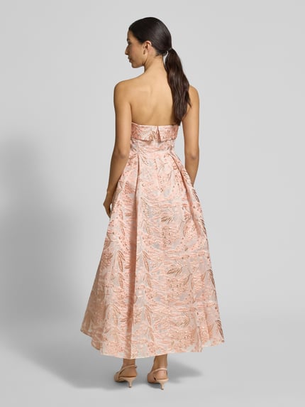 Frauenmodel trägt Regular Fit Midikleid mit floralem Allover-Stitching von Adrianna Papell in Apricot, A-Linie, Schulterfrei, Kellerfalten, Nahtreißverschluss, Ganzkörperansicht Rückansicht.