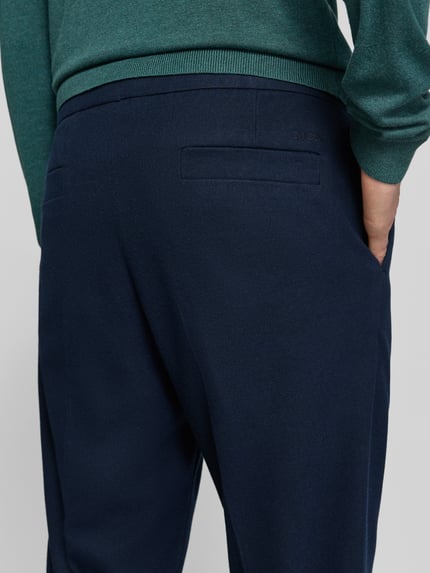 Männermodel trägt Regular Fit Bundfaltenhose mit Seitenriegel von MCNEAL in Dunkelblau, weiche Textur, Nahaufnahme Rückansicht, Herren Bundfaltenhose, 1er-Bundfalte, Eingrifftaschen, Gesäßtaschen, Bundweite 45 cm, Innenbeinlänge 78 cm.
