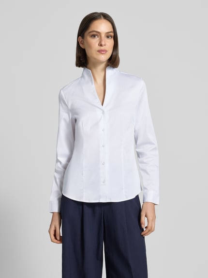 Frauenmodel trägt Hemdbluse mit Stehkragen und V-Ausschnitt von Christian Berg Woman, weiß, Baumwoll-Mix mit Stretch-Anteil, taillierter Schnitt, Knopfleiste, Ganzkörperansicht von vorne.