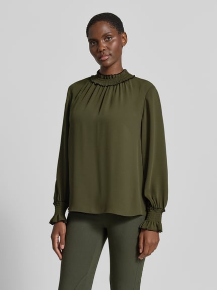 Kobiece model nosi Loose Fit Langarmbluse mit Mock Neck od Marc Cain z szyfonu, krój regular fit, stójka, marszczone detale, Długość tyłu w rozmiarze 36: 61 cm, Długość rękawów w rozmiarze 36: 63 cm, odcień oliwkowy, gładka tekstura, Ganzkörperansicht von vorne.