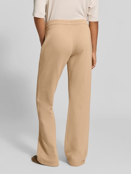 Frauenmodel trägt Sweatpants aus Baumwoll-Modal-Mix von Juvia in Beige, lockere Passform, Fleece-Innenseite, Rückansicht, Ganzkörperansicht.