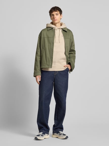 Mannelijk model draagt Regular Fit Hoodie aus Baumwoll-Mix van Tommy Jeans, effen, logo-stitching, staande kraag met capuchon, fleece katoenmix, lange mouw, geribde zoom, Ganzkörperansicht von vorne.