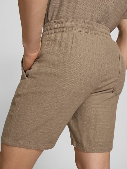Männermodel trägt Regular Fit Shorts aus Viskose-Leinen-Mix Modell 'TEL LATHAM' von Only & Sons, beige, strukturierte Oberfläche, Nahaufnahme Rückansicht.