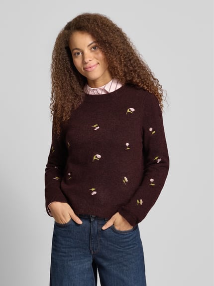 Vrouwenmodel draagt Regular fit pullover met wol-aanteil model 'SHINE' van ONLY, look: effen, bloemenmotief, bloemenborduursel, ronde hals, lange mouwen, mouwboord, gebreide verwerking, donkerrood met geborduurde bloemen, detailopname bovenlichaam.