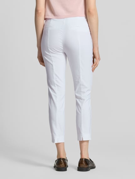 Frauenmodel trägt Slim Fit Stoffhose in verkürzter Passform von Christian Berg Woman in Weiß, glatte Textur, ganzkörperansicht Rückansicht. Elastischer Baumwoll-Mix, Knopf- und Reißverschluss, Produktdetails laut Kontext.