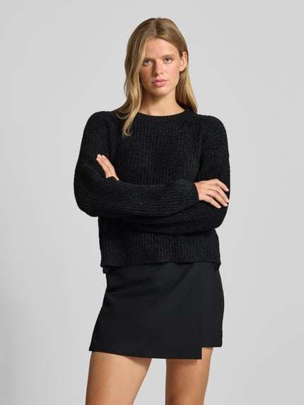 Frauenmodel trägt Relaxed Fit Strickpullover mit elastischen Abschlüssen von REVIEW, schwarze Farbe, strukturierte Oberfläche, lockere Passform, Rundhalsausschnitt, Damenmodell, Ganzkörperansicht von vorne.