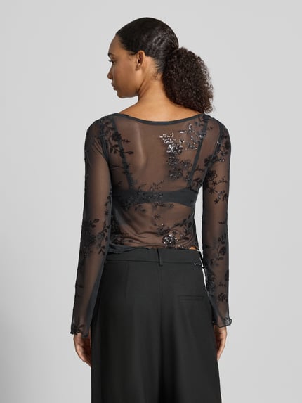 Frauenmodel trägt Langarmshirt mit ausgestelltem Ärmelabschluss von PIECES in Schwarz mit floralem Allover-Spitzenmuster aus Mesh, Ganzkörperansicht Rückansicht.