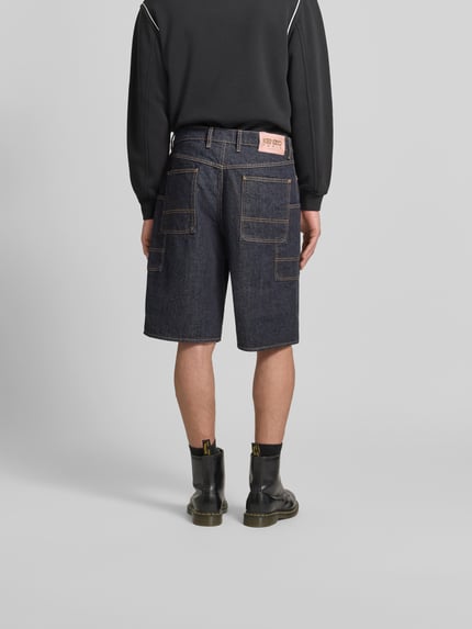 Mannenmodel draagt Straight Fit Shorts in Denim-Optik van Kenzo, puur katoen, cargozak, knoop- en ritssluiting, denimlook, binnenbeenlengte 46 cm, bandwijdte 28 cm, ganzebodyshot achteraanzicht.